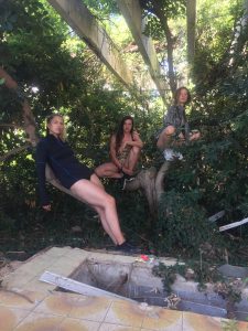 Three women sit in and lean against a tree. They wear short sporty clothes.