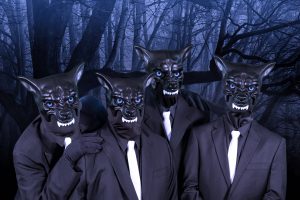 Vier Menschen in schwarzen Anzügen. weißen Kravatten und mit Hundemasken stehen im Wald. Es ist dunkel.
